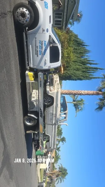 Fast Hook Towing flatbed transporting a sedan on a palm-lined street